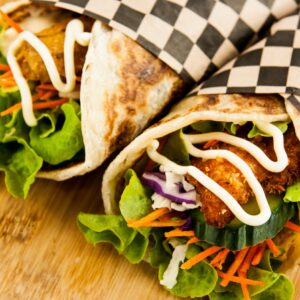 Close-up of chicken wraps with lettuce, cucumber, carrots, and mayo on wooden surface.